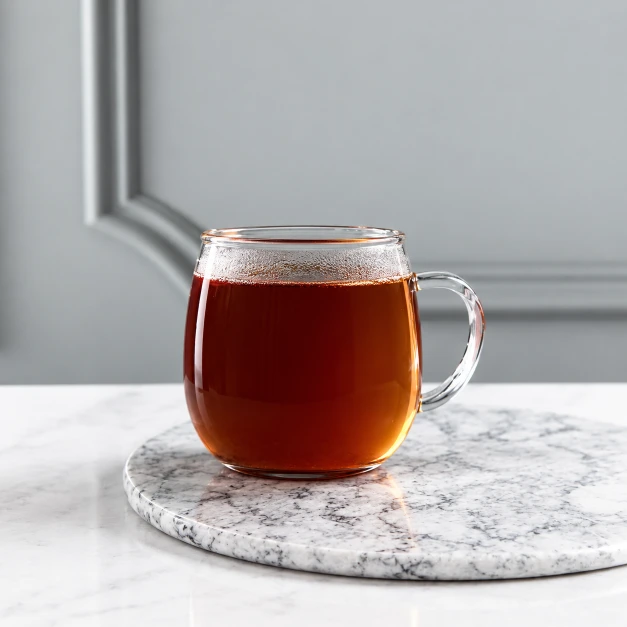 Alt: Transparent glass cup filled with warm amber tea.
